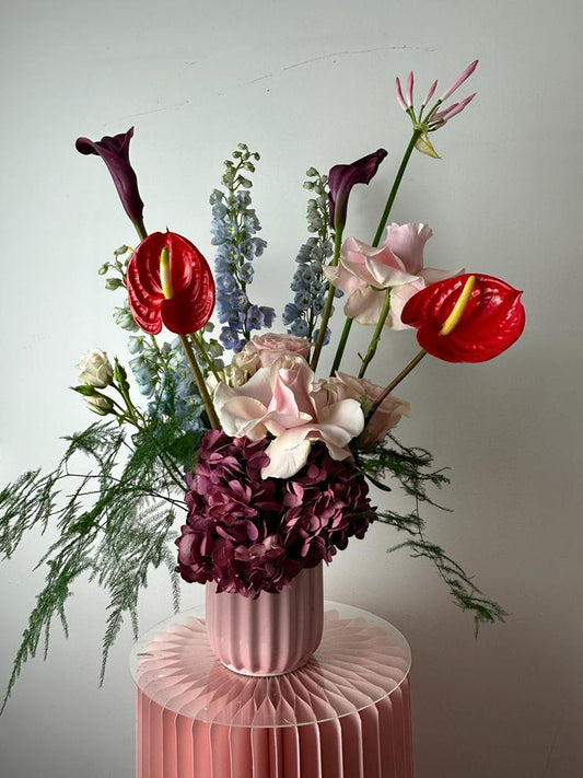 scultural floral vase arrangement with bold colours on a pink plinth.